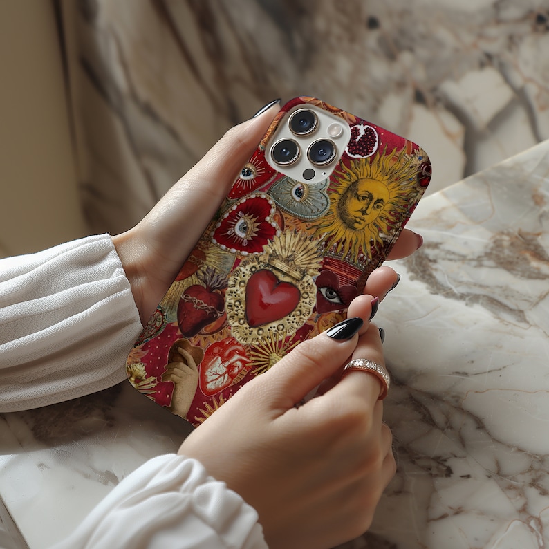 May include: A red, gold and white iPhone case featuring a collage of religious imagery, including hearts, eyes and a sun with a face. The case has a camera lens cutout.
