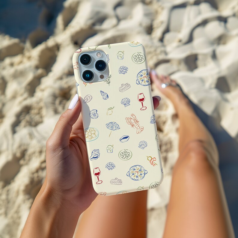 May include: A white iPhone case with a pattern of various Italian food items, including pasta, wine glasses, and seafood. The case is being held by a person's hand.