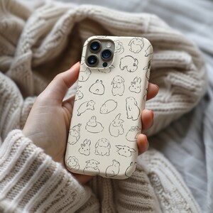 K&ouml;nnte beinhalten: Eine wei&szlig;e iPhone-H&uuml;lle mit einem Muster aus schwarzen Kaninchen. Die H&uuml;lle hat einen Ausschnitt f&uuml;r das Kameraobjektiv und einen schwarzen Rand.