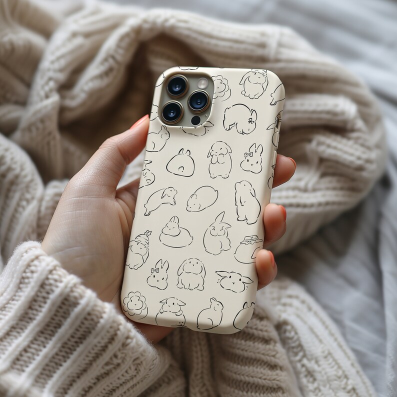 K&ouml;nnte beinhalten: Eine wei&szlig;e iPhone-H&uuml;lle mit einem Muster aus schwarzen Kaninchen. Die H&uuml;lle hat einen Ausschnitt f&uuml;r das Kameraobjektiv und einen schwarzen Rand.