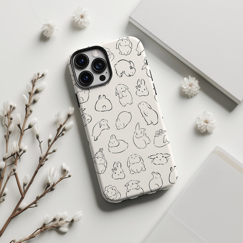 K&ouml;nnte beinhalten: Eine wei&szlig;e iPhone-H&uuml;lle mit einem schwarz-wei&szlig;en Muster aus Kaninchen. Die H&uuml;lle hat einen Ausschnitt f&uuml;r das Kameraobjektiv und einen wei&szlig;en Hintergrund.