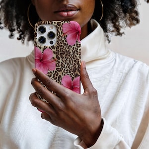 May include: A phone case featuring a leopard print and pink hibiscus flowers. The case is designed for a phone with a triple lens camera.