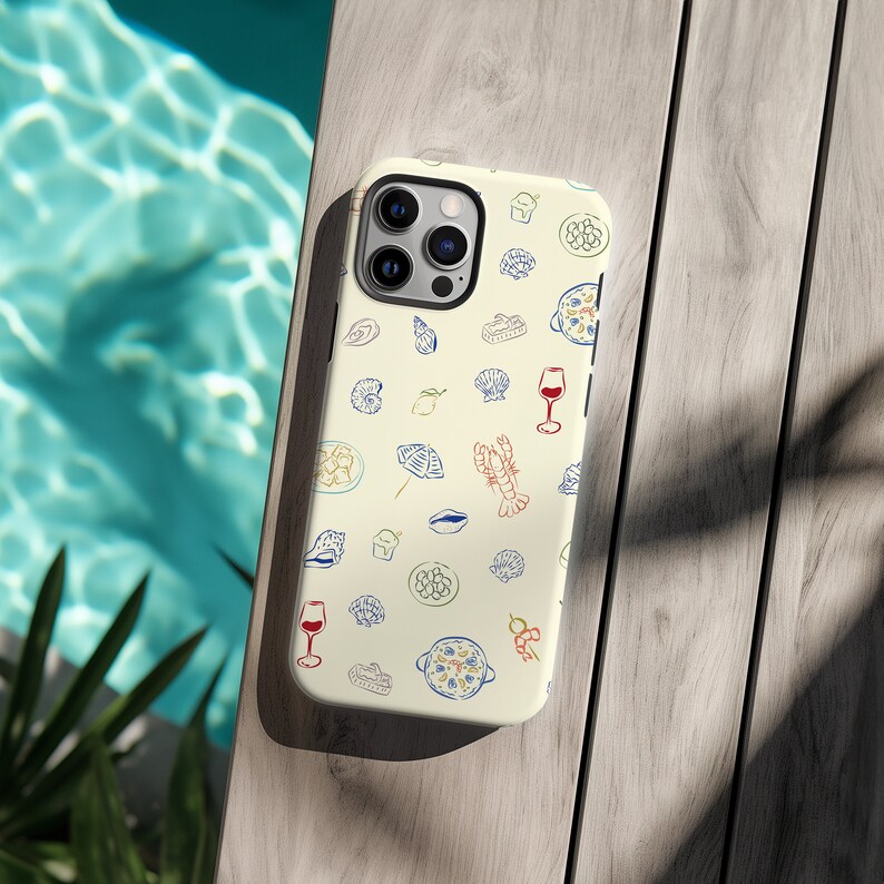 May include: A white iPhone case with a colorful pattern of seafood, lemons, and wine glasses. The case has a camera cutout and a white background.