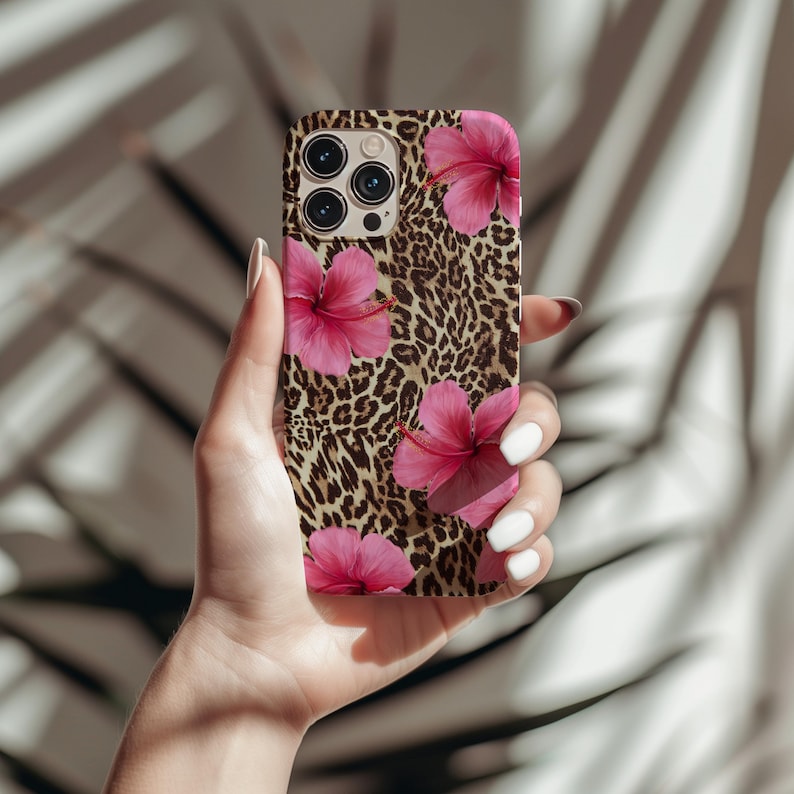 May include: A phone case featuring a leopard print background and pink hibiscus flowers. The case has a camera lens cutout and a black border.