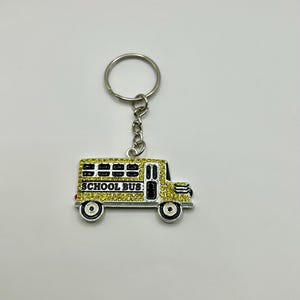 May include: A yellow school bus keychain with black accents and the words "SCHOOL BUS" in black. The keychain has a silver key ring and chain. The bus is decorated with yellow rhinestones.