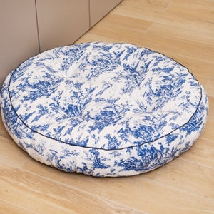 May include: A round, white and blue patterned pet bed with a black trim. The bed is filled with a soft, comfortable material.