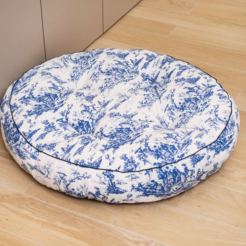 May include: A round, white and blue patterned pet bed with a black trim. The bed is filled with a soft, comfortable material.