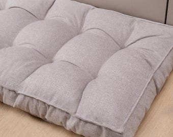 May include: A rectangular floor cushion in a light gray, textured fabric. The cushion features a tufted design with multiple stitched indentations creating a grid of soft, raised sections across the surface, providing a uniform, padded appearance.
