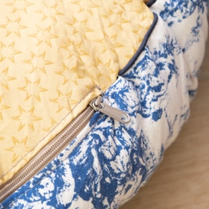 May include: A yellow fabric cushion with a zipper closure. The cushion has a star pattern and is sewn to a blue and white fabric with a floral pattern.