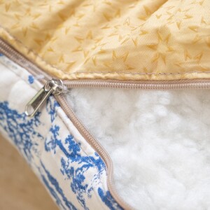 May include: A close-up of a zipper on a pillow with a white and blue floral pattern on one side and a yellow fabric with a star pattern on the other side.