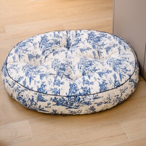 May include: A round, white and blue patterned floor cushion with a dark blue trim. The cushion is filled with a soft, comfortable material.