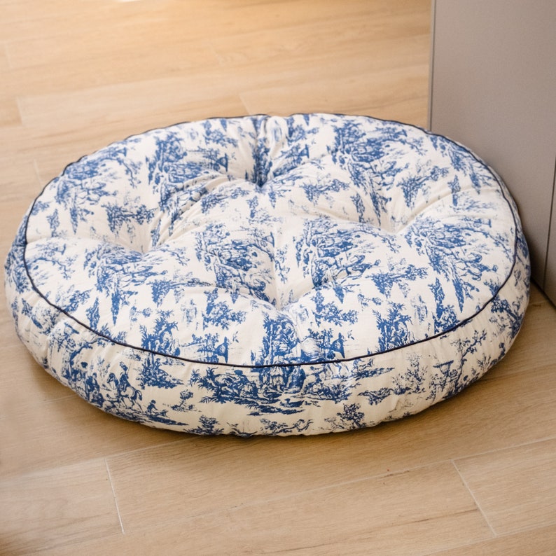 May include: A round, white and blue patterned floor cushion with a dark blue trim. The cushion is filled with a soft, comfortable material.
