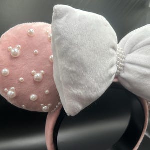 May include: Pink velvet Minnie Mouse ears with a white bow and pearl embellishments.