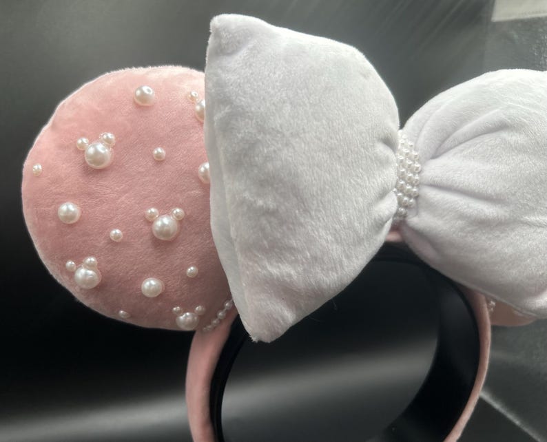 May include: Pink velvet Minnie Mouse ears with a white bow and pearl embellishments.