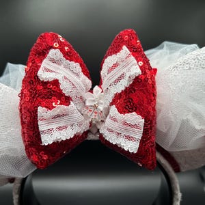 May include: Red and white sequined Minnie Mouse ears with a white lace bow and a white tulle overlay.