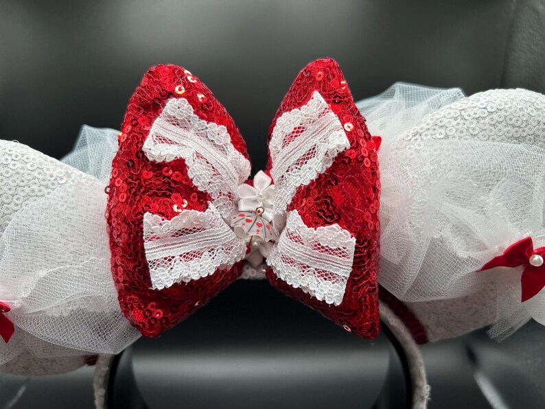 May include: Red and white sequined Minnie Mouse ears with a white lace bow and a white tulle overlay.