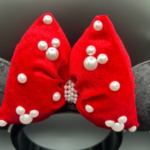 K&ouml;nnte beinhalten: Rotes Samt-Minnie-Maus-Ohrenband mit einer gro&szlig;en Schleife, die mit wei&szlig;en Perlen verziert ist. Die Schleife hat zwei Mickey-Maus-Formen aus Perlen.