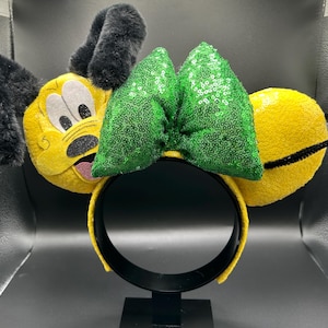 Può includere: Orecchie di personaggio gialle con orecchie nere e soffici e un fiocco verde con paillettes. La fascia è gialla e nera. Il volto del personaggio è giallo con dettagli neri e bianchi.