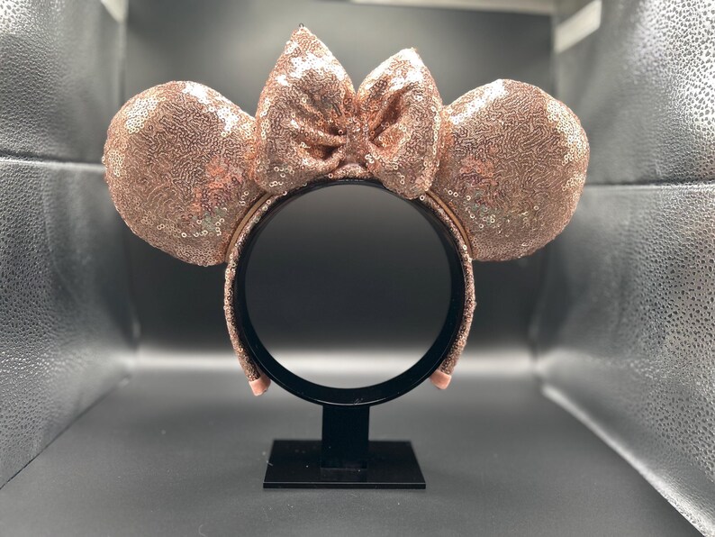 May include: Rose gold sequined mouse ear headband with a matching bow. The ears and bow are covered in shimmering sequins. The headband is black and has a rose gold band. A fun accessory for themed events.