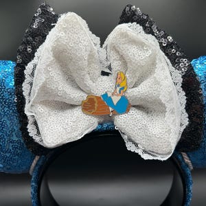 May include: Blue sequined mouse ears with a white sequined bow and black sequined accents. A small pin of Alice from Alice in Wonderland is attached to the bow. The headband is black.