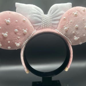 May include: Pink velvet mouse ears headband with a white bow and pearl embellishments.