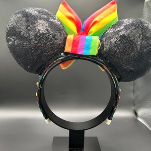 K&ouml;nnte beinhalten: Schwarze, mit Pailletten besetzte Minnie Mouse Ohren mit einer Regenbogen Schleife. Das Stirnband ist mit bunten Perlen verziert.