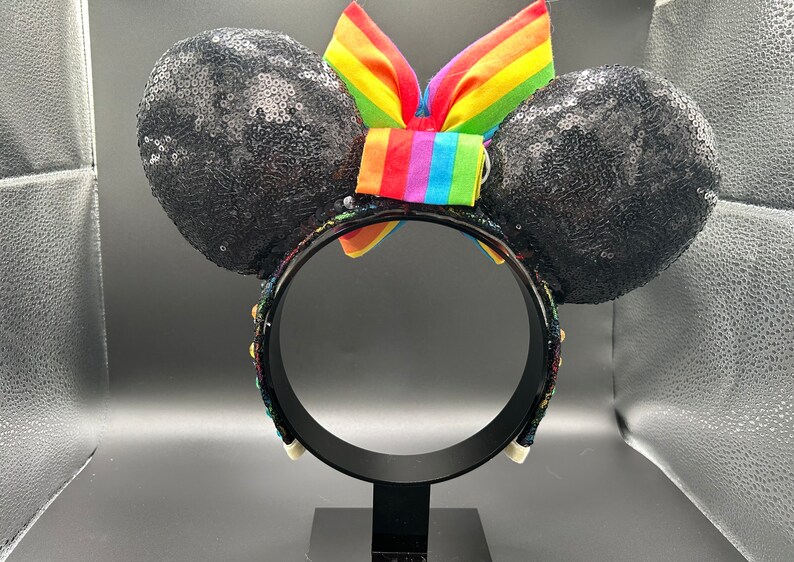 K&ouml;nnte beinhalten: Schwarze, mit Pailletten besetzte Minnie Mouse Ohren mit einer Regenbogen Schleife. Das Stirnband ist mit bunten Perlen verziert.