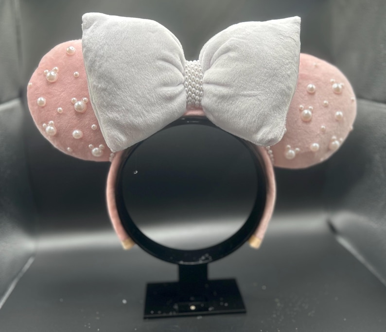 May include: Pink Minnie Mouse ears with a white velvet bow and pearl embellishments.