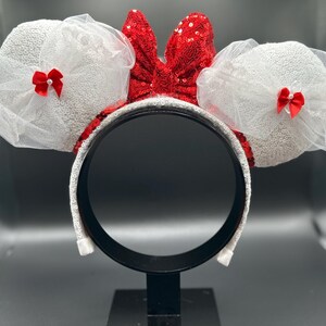 May include: White sparkly Minnie Mouse ears with a red sequined bow and white tulle.