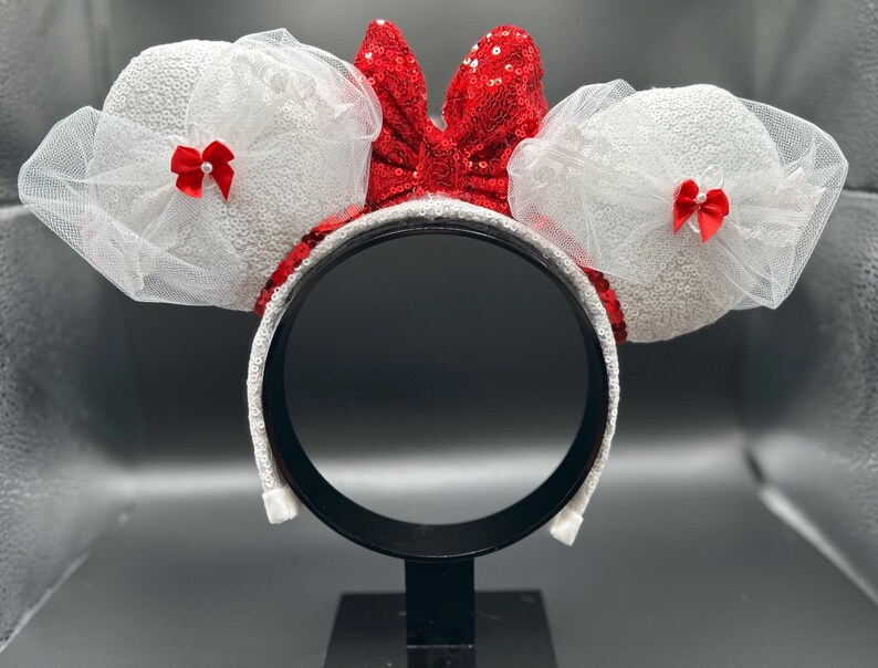 May include: White sparkly Minnie Mouse ears with a red sequined bow and white tulle.