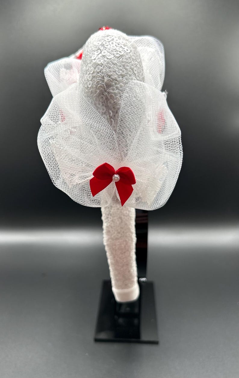 May include: White headband with a white tulle bow and a red satin bow. The headband is decorated with sequins.