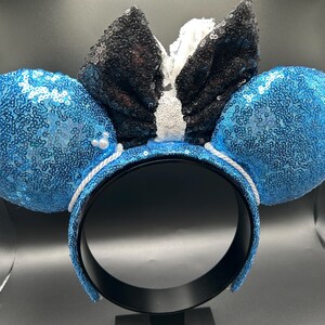 May include: A pair of mouse ears with blue sequined ears and a black sequined bow with white accents. The headband is black with a white rope detail. A fun accessory for themed events.