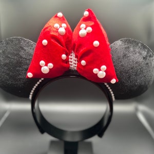K&ouml;nnte beinhalten: Roter Samt-Schleife mit wei&szlig;en Perlenbesatz auf einem schwarzen Haarreif. Die Schleife ist in Form von Minnie Mouse Ohren.