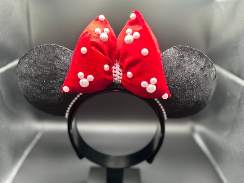 K&ouml;nnte beinhalten: Roter Samt-Schleife mit wei&szlig;en Perlenbesatz auf einem schwarzen Haarreif. Die Schleife ist in Form von Minnie Mouse Ohren.