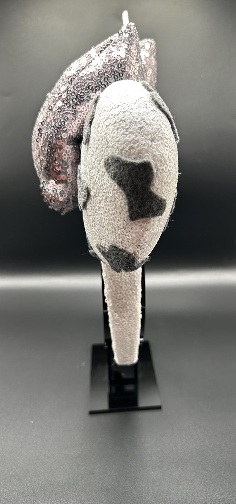 May include: A headband featuring two round ears covered in white sequins with dark grey felt patches. A large, upright bow covered in shimmering silver sequins is attached between the ears. The headband itself is also covered in white sequins.