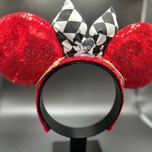 May include: Red sequined Minnie Mouse ears with a black and white checkered bow. The bow has a small black and white character in the center.