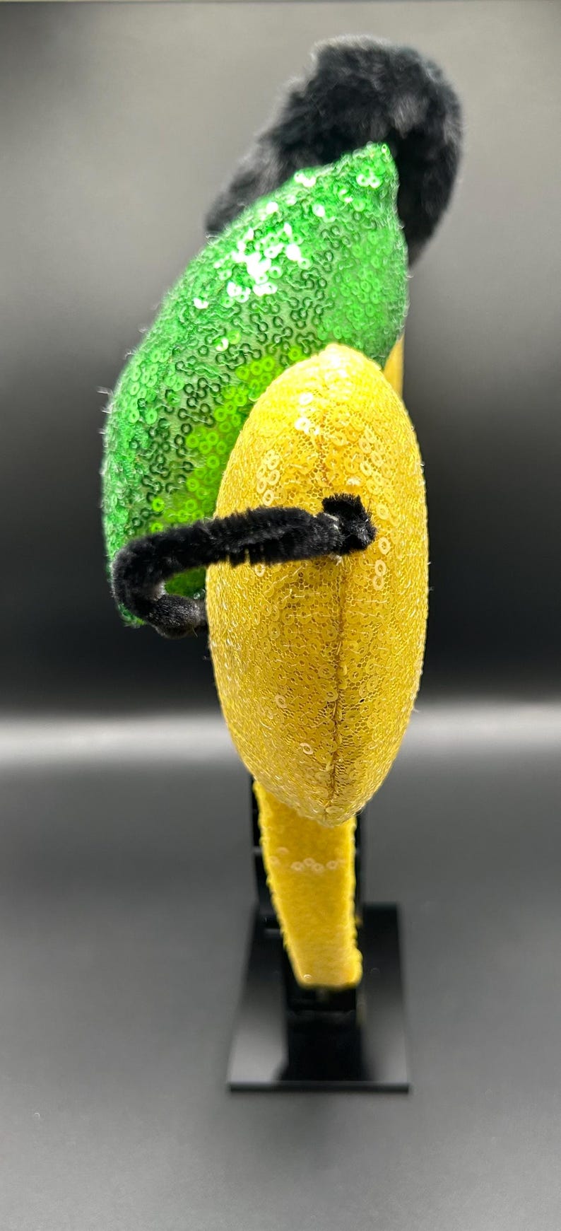 May include: A whimsical headband featuring a black faux fur accent, a vibrant green sequined section, and a yellow sequined section. A black fuzzy wire adds a playful touch. This accessory is perfect for themed events.