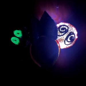 May include: A dark image featuring a glowing green element, a black shape, and a circular object with a spiral design. The circular object has a red outline and a white center. The background is dark with hints of purple.