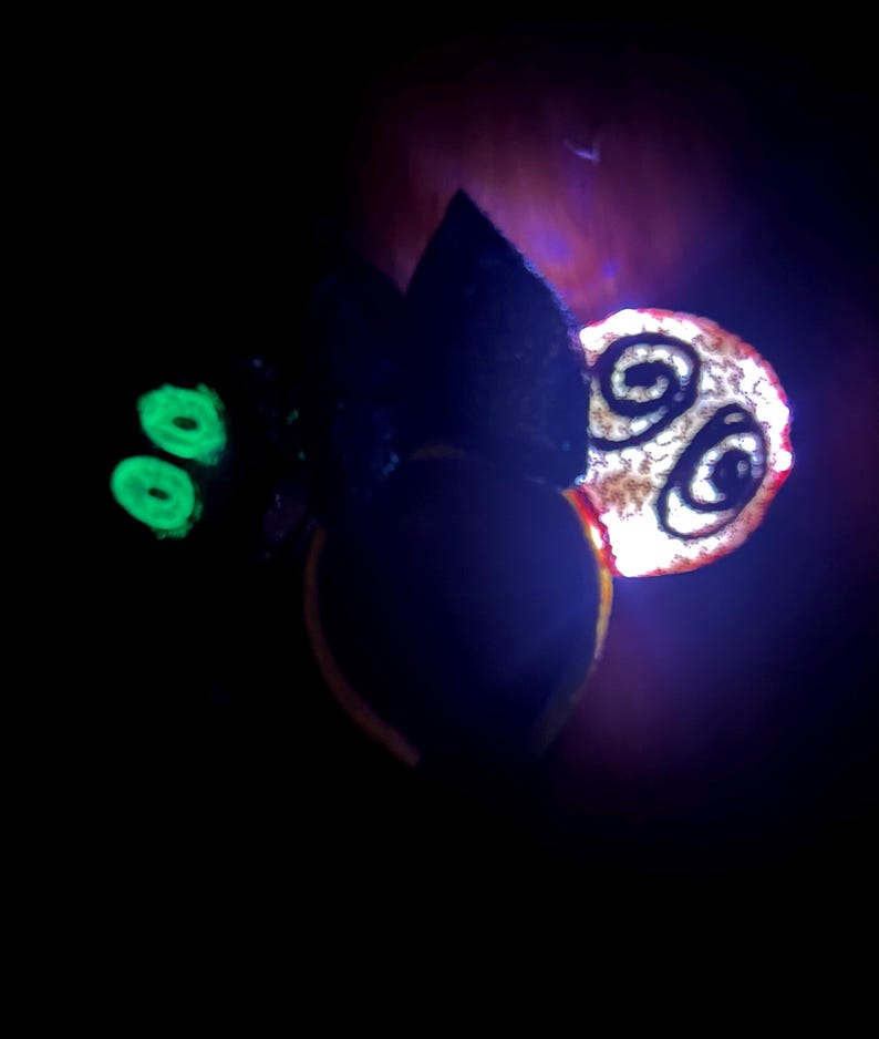 May include: A dark image featuring a glowing green element, a black shape, and a circular object with a spiral design. The circular object has a red outline and a white center. The background is dark with hints of purple.