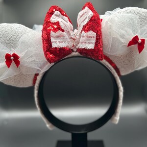 May include: White mouse ears headband with a red bow and white tulle. The bow has white lace trim and a red sequined center.