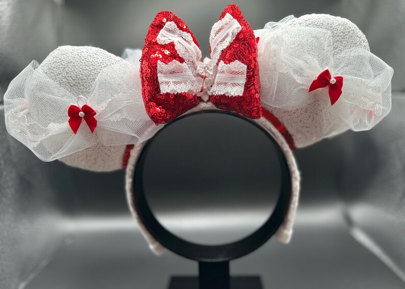 May include: White mouse ears headband with a red bow and white tulle. The bow has white lace trim and a red sequined center.