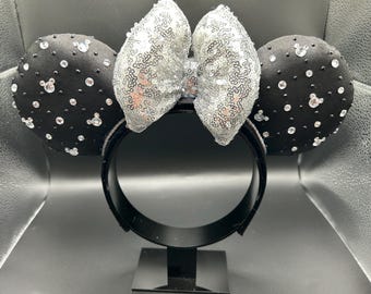 Cerchietto con orecchie di Minnie Mouse illuminate da cristalli neri e fiocco di paillettes argentate.