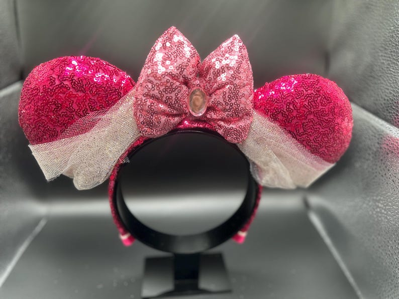 Op de afbeelding: Roze en witte Minnie Mouse oren met pailletten, met een roze strik en een heldere strasssteen in het midden.
