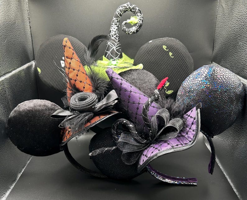 May include: A collection of Halloween-themed headbands featuring black, purple, and orange witch hats, bows, and ears. Some ears have a textured, glittery appearance. The headbands are decorated with feathers and lace, creating a festive and spooky look.