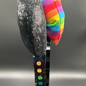K&ouml;nnte beinhalten: Schwarze Pailletten-Minnie-Maus-Ohren mit einer regenbogenfarbenen Schleife aus Stoff. Das Stirnband ist mit regenbogenfarbenen Edelsteinen verziert.