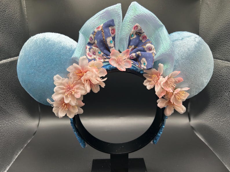 Peut inclure: Un serre-t&ecirc;te avec deux grandes oreilles en velours bleu clair, un n&oelig;ud central bleu clair iris&eacute; et un n&oelig;ud en tissu violet &agrave; motif floral. Le serre-t&ecirc;te est orn&eacute; de grappes de fleurs de cerisier artificielles rose p&acirc;le.