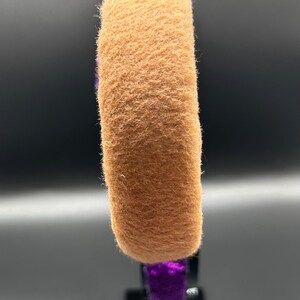 Op de afbeelding: Een haarband met een dikke, beige, pluizige stoffen band die contrasteert met paarse paillettenstof op de rest van het frame. Het ontwerp toont een duidelijk textuurverschil tussen het zachte, matte beige materiaal en de reflecterende, glanzende paarse pailletten.