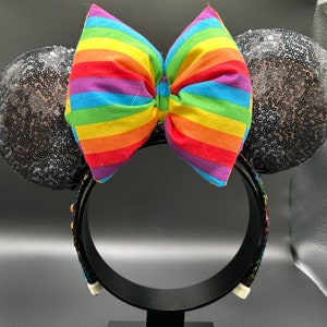 K&ouml;nnte beinhalten: Schwarze Pailletten-Minnie-Maus-Ohren mit einer regenbogenfarbenen Schleife.