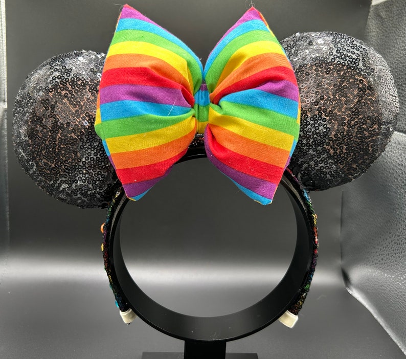K&ouml;nnte beinhalten: Schwarze Pailletten-Minnie-Maus-Ohren mit einer regenbogenfarbenen Schleife.