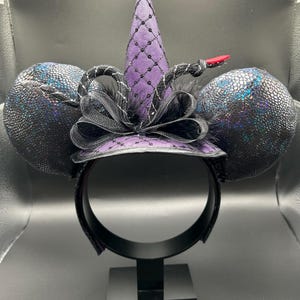 May include: A black headband with two large, textured, iridescent black ears. A purple witch hat with a black net overlay and a black bow sits atop the headband. A black and silver snake with a red tongue is wrapped around the hat.
